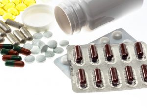 Assorted pharmaceutical tablets and capsules spilling from a bottle beside blister packs