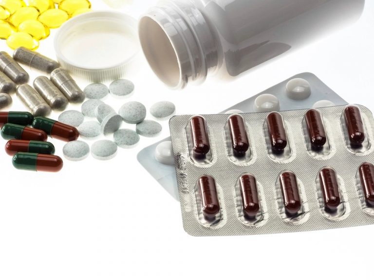 Assorted pharmaceutical tablets and capsules spilling from a bottle beside blister packs