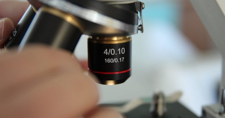 Close up of a microscope objective lens positioned over a specimen slide in a laboratory