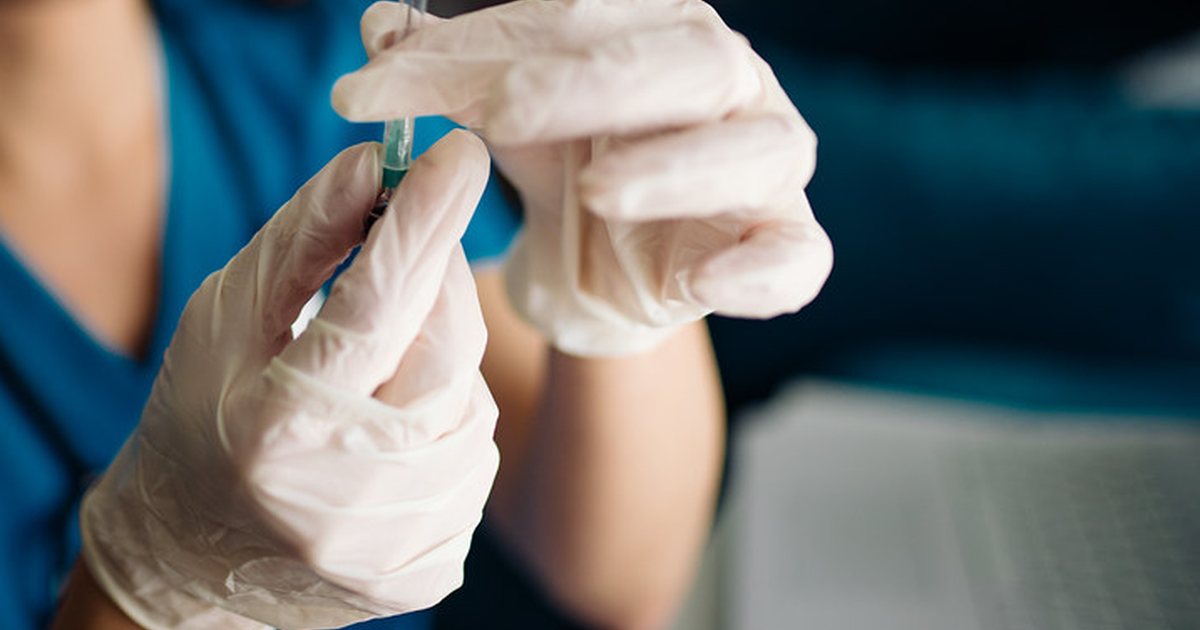 Gloved hands drawing liquid into a syringe from a small vial