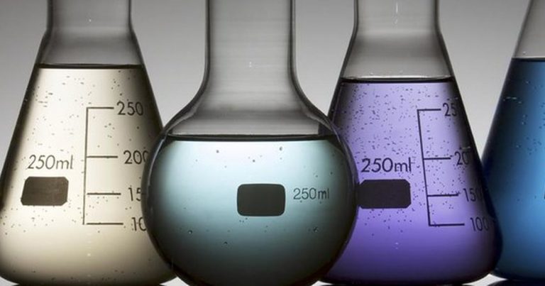 Three glass laboratory flasks with graduation markings holding clear, green and purple solutions