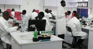 Row of researchers in white coats working at microscopes along a laboratory bench