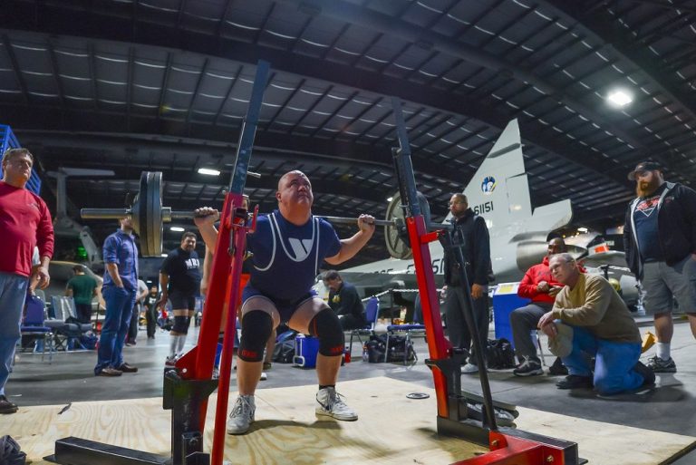 Powerlifter performing a heavy barbell back squat in a squat rack at a competition