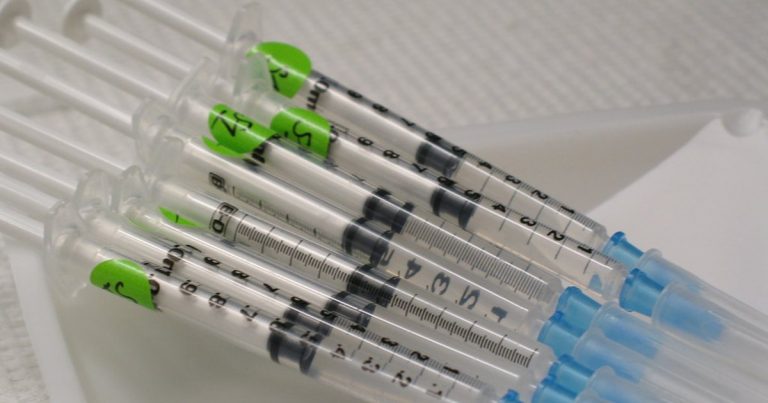 Several prepared graduated syringes with colored caps laid out in a row on a white laboratory surface