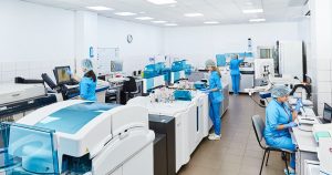 Wide view of a modern clinical laboratory with automated analyzers and staff in blue scrubs at workstations
