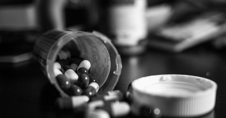 White tablets spilling out of an open medicine bottle onto a dark surface