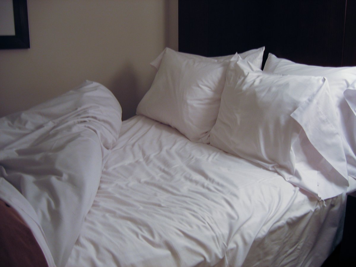 White pillows and bedding on a made bed in low light