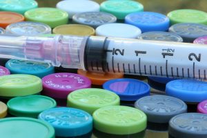 A syringe resting on a tray of colored vial caps in a laboratory